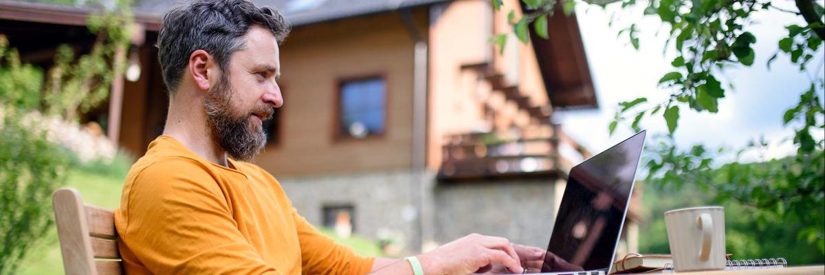 Mann sitzt im Garten am Laptop.