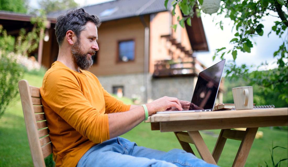 Mann sitzt im Garten am Laptop.